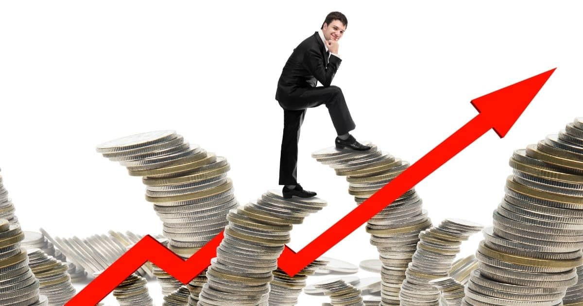 A man in a business suit walks on piles of coins intertwined with a red arrow trending upward