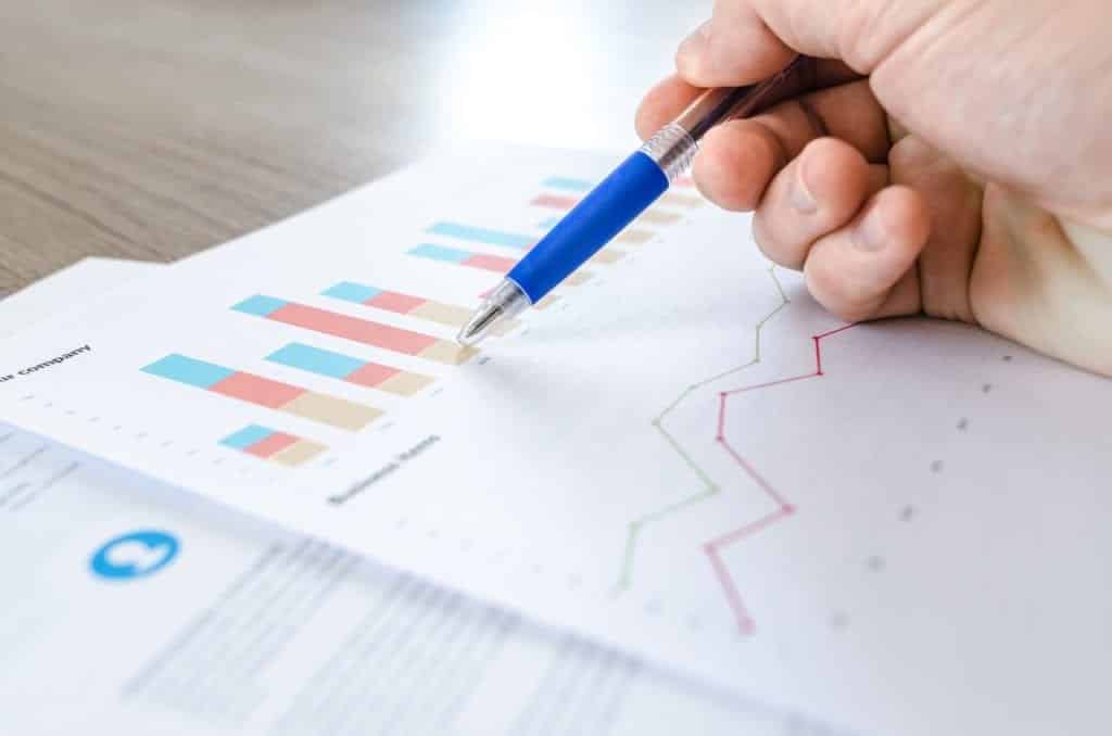 A hand holding a pen pointing at business documents with graphs