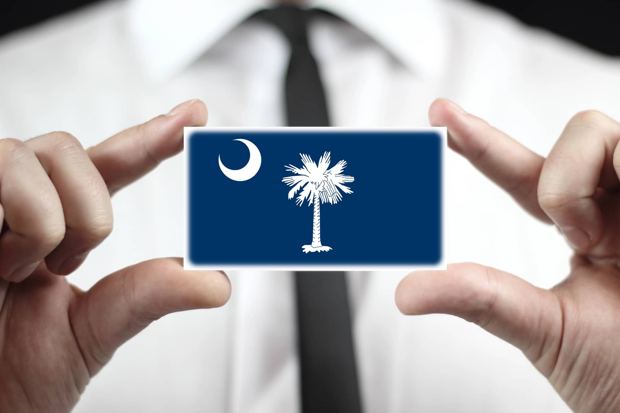 Man with a tie holding a card of the South Carolina flag