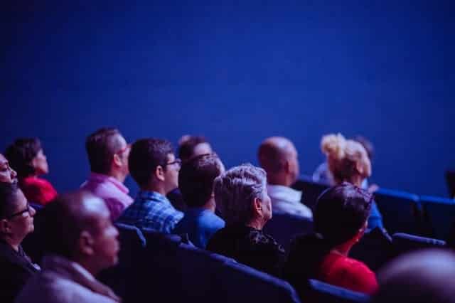 People in an audience sitting and listening to a speaker at a conference