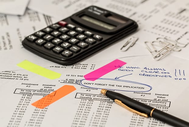 A calculator on top of financial documents with a pen