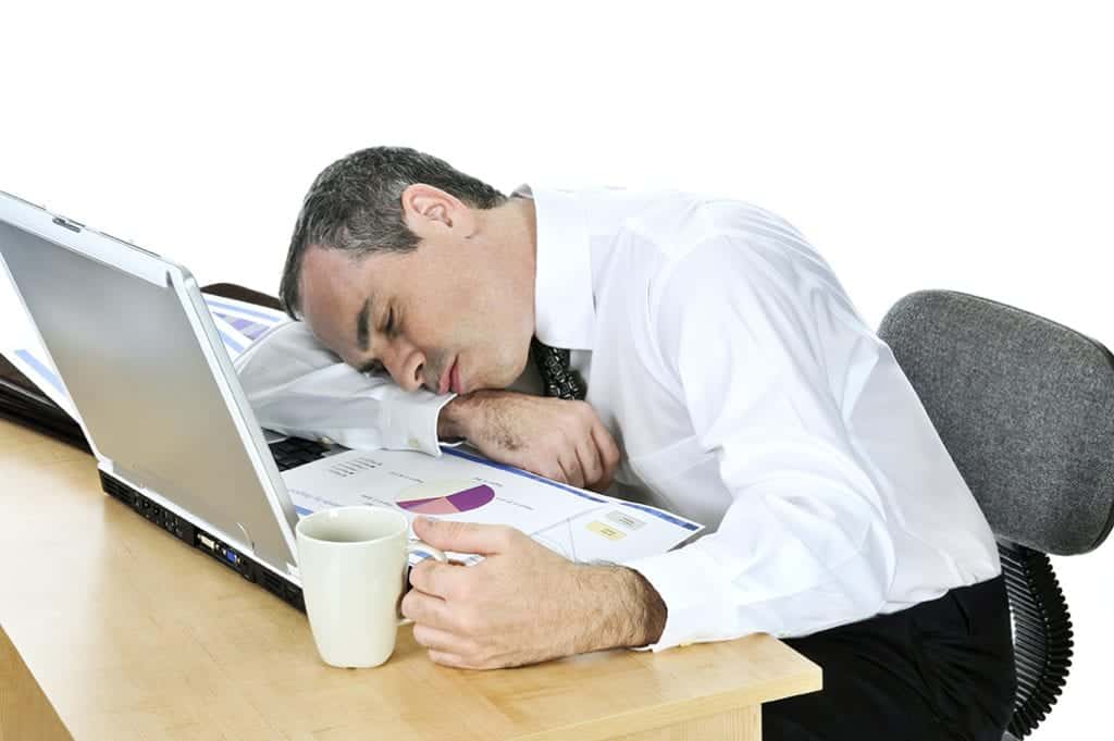 A business man asleep clutching a cup of coffee in front of his computer